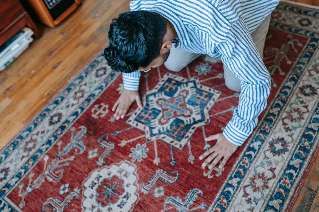 A Muslim man in prayer position on an ornate rug in a cozy indoor setting.