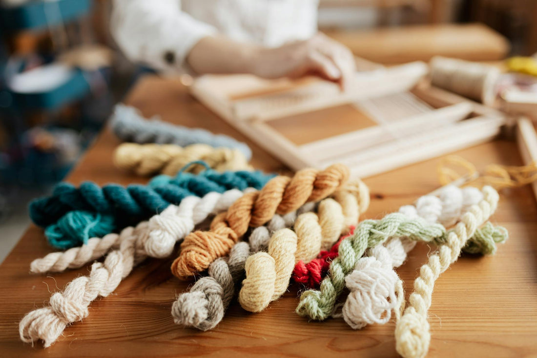 Close-up of vibrant yarn skeins spread on a wooden table with weaving in progress.
