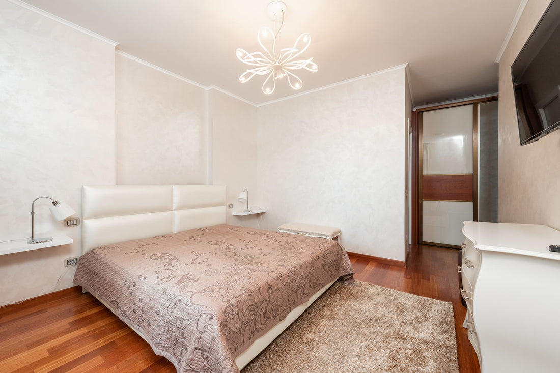 Interior of spacious bedroom with comfortable bed and modern TV hanging on wall above classic styled white commode