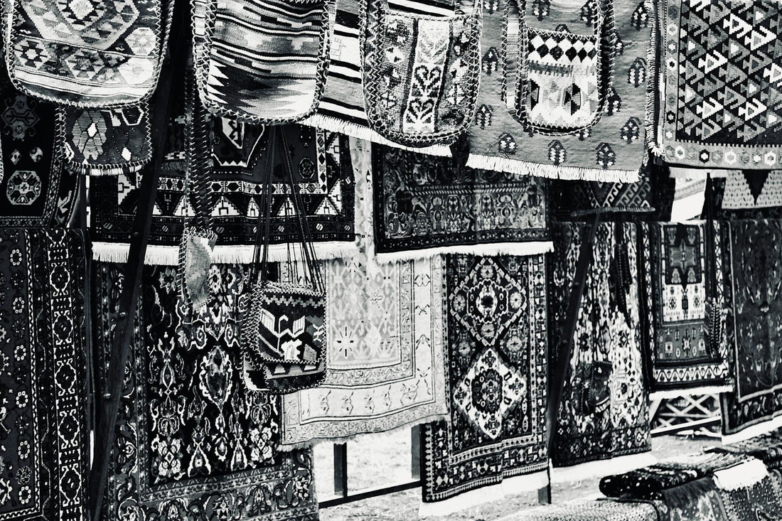 A collection of traditional handmade rugs with intricate patterns and designs displayed in an outdoor market.