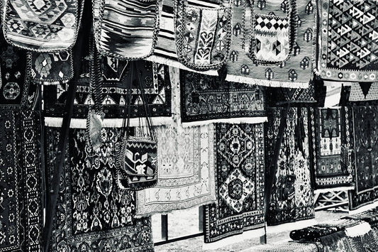 A collection of traditional handmade rugs with intricate patterns and designs displayed in an outdoor market.
