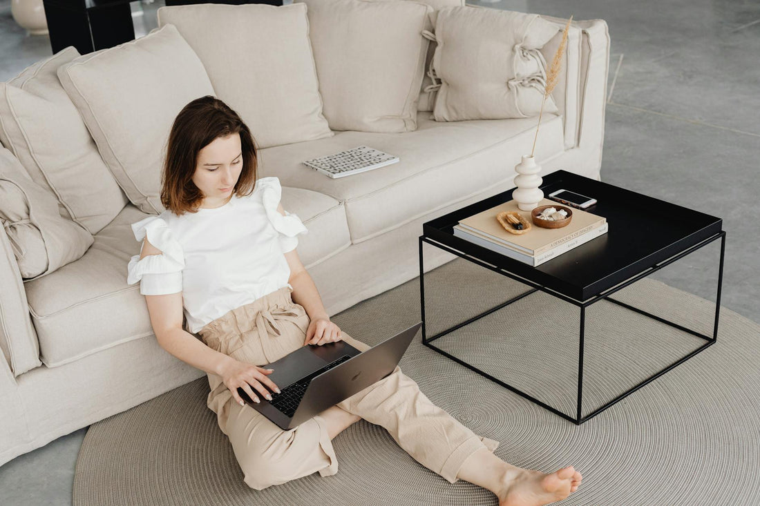 A woman sits comfortably on the floor working on her laptop in a modern living room.