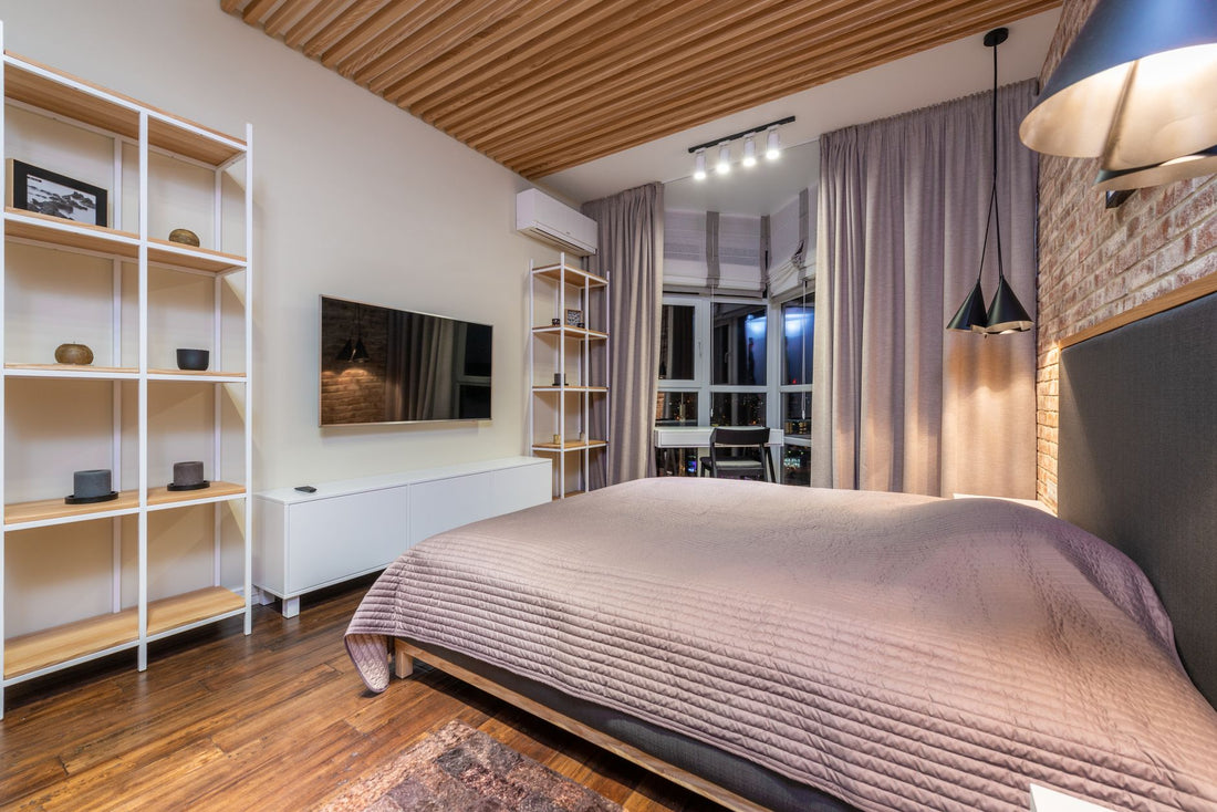 Bed against shelves and cabinet under television reflecting brick wall with lamps in modern house with parquet