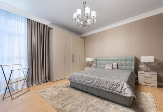 Bed with coverlet and cushions against lamps on bedside tables on parquet under chandelier in light house