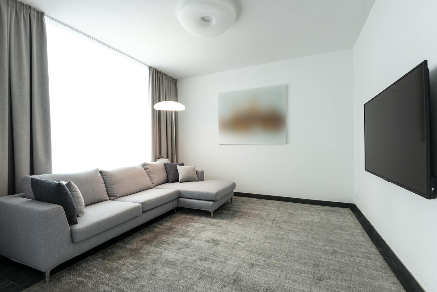 Spacious modern living room with L-shaped grey sofa and flat-screen TV in a minimalist design.