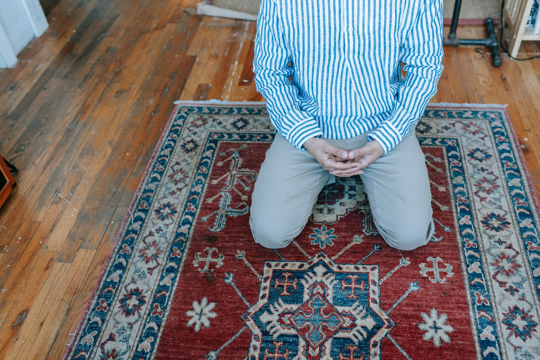 Man kneeling on an intricately designed rug, symbolizing religious prayer in a peaceful indoor setting.