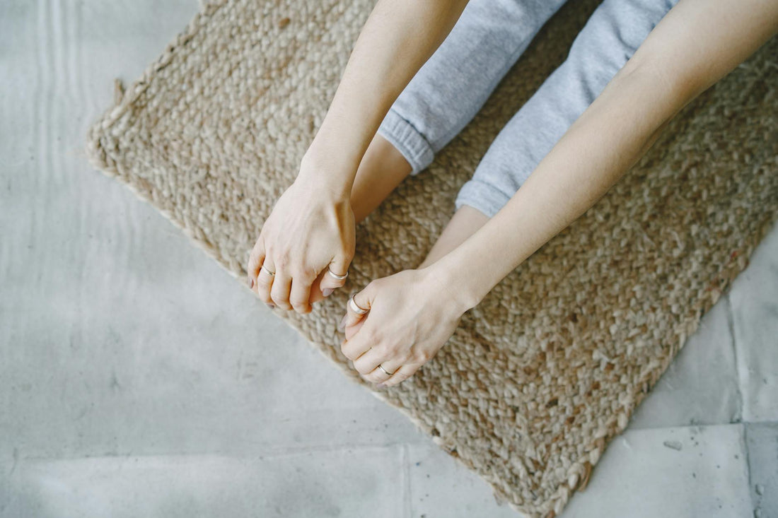 A person stretching on a woven mat. Close-up view of hands and feet in relaxed yoga pose.