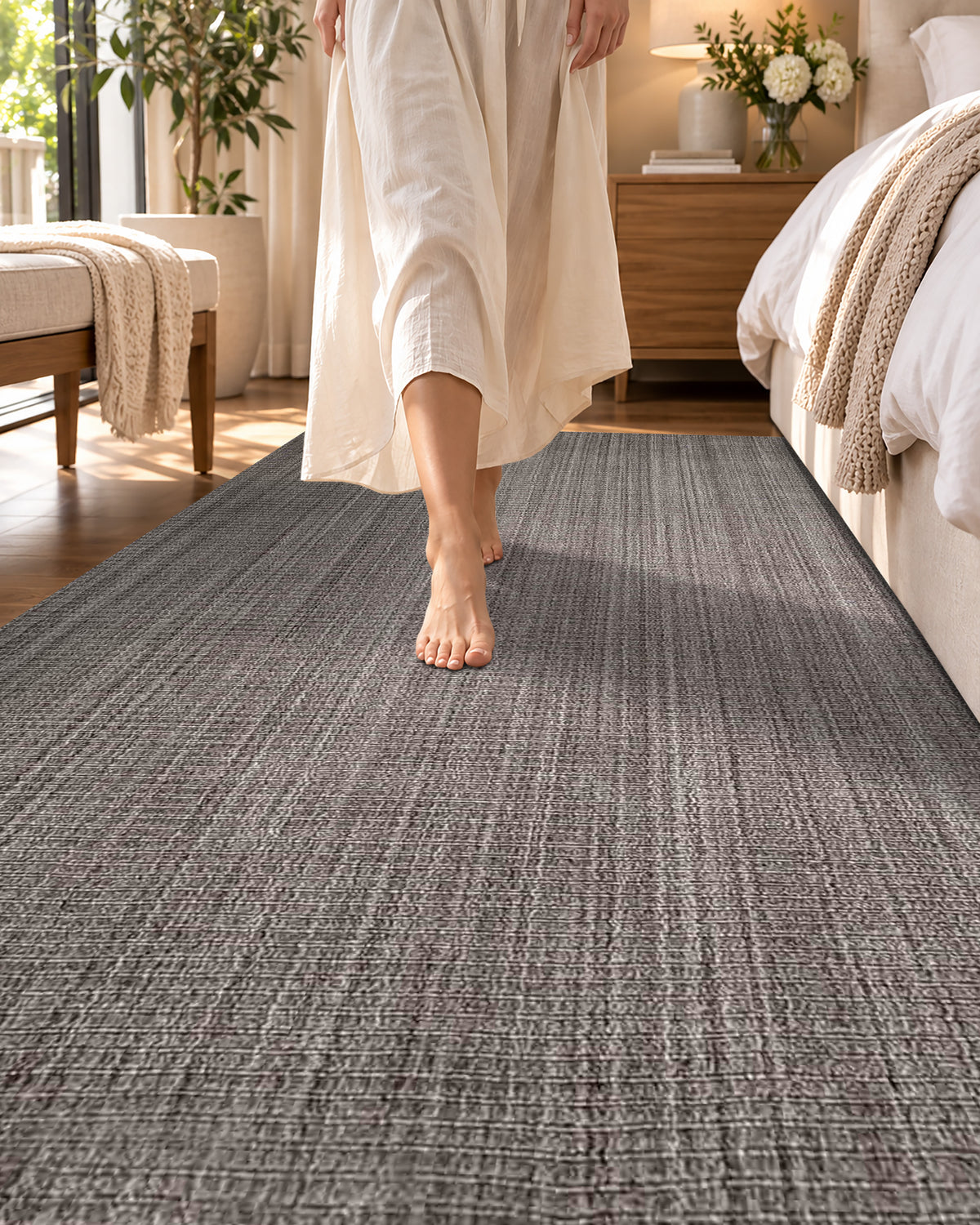 Artisan Carey Brown Style Shot — Close-up of a textured brown rug with a barefoot woman walking beside the bed.