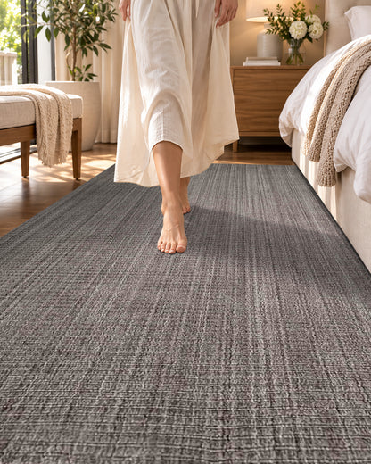 Artisan Carey Brown Style Shot — Close-up of a textured brown rug with a barefoot woman walking beside the bed.