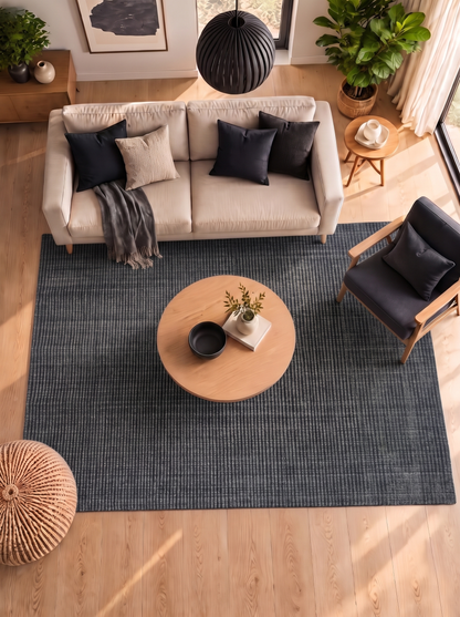 Artisan Carey Charcoal Living Room Overhead Shot — Overhead view of a charcoal striped rug beneath a round wooden coffee table.