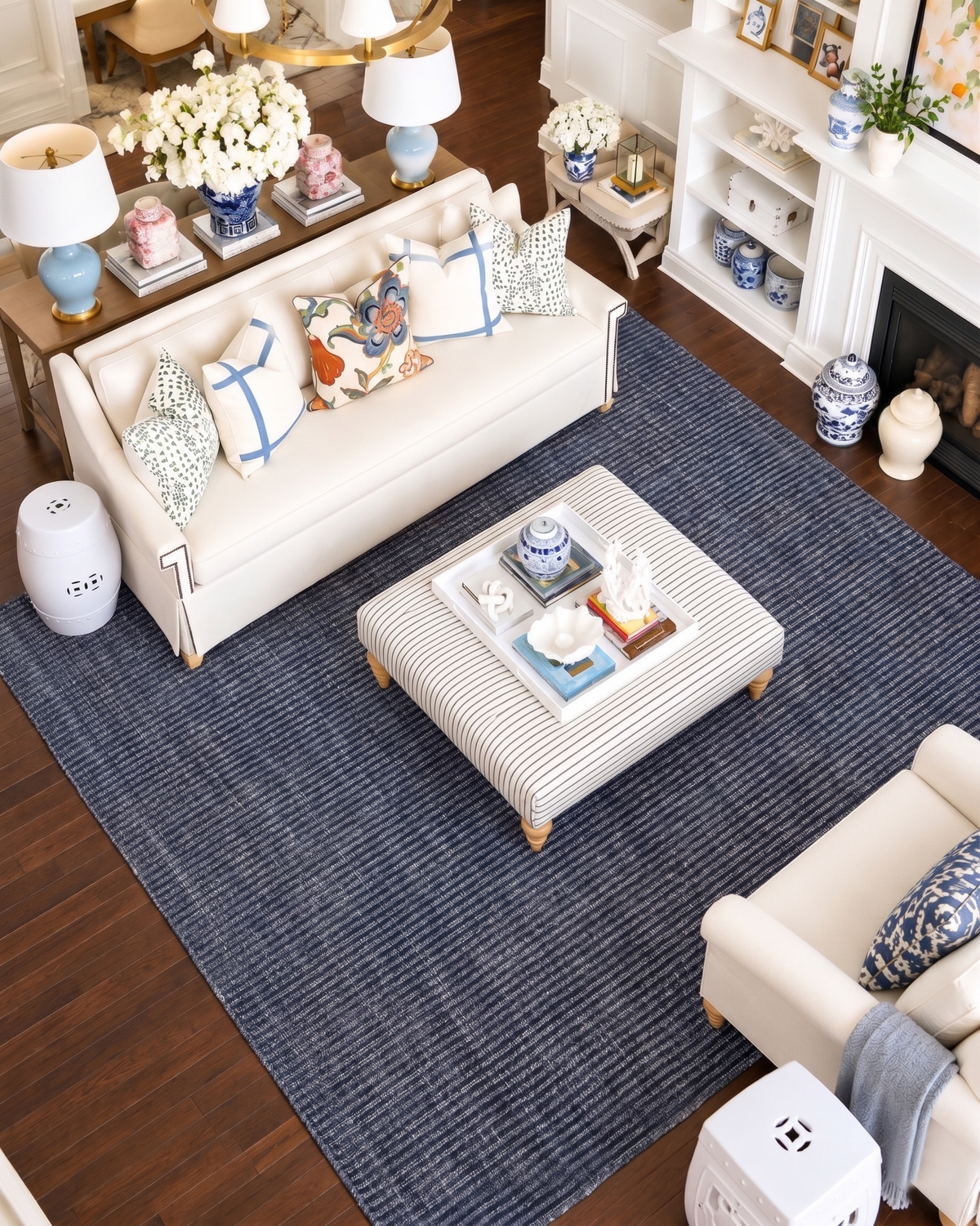 Artisan Carey Navy Living Room Overhead Shot — Overhead view of a textured navy rug beneath a striped ottoman and cream seating.