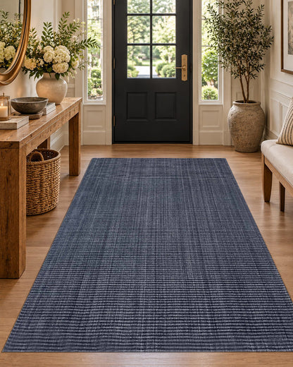 Artisan Carey Navy Style Shot — Navy rug with subtle linear texture in an entryway with a wood console and bench.