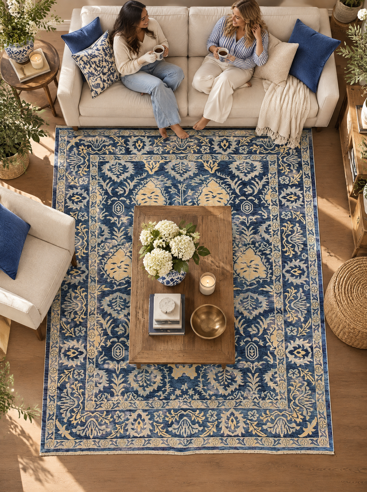 Artisan Emma Navy Style Shot — Navy floral rug beneath a wooden coffee table, with two women seated nearby.