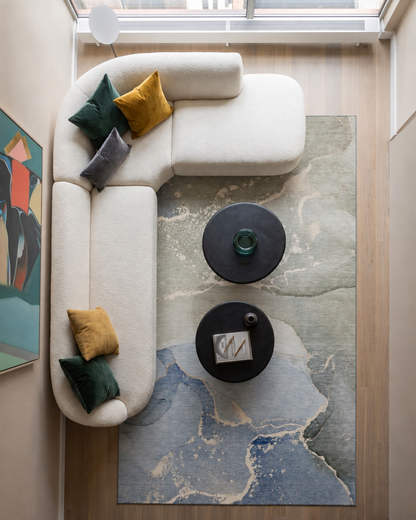 Dalyn Rugs Odyssey OY10 Sky Overhead Shot — Overhead view of a blue and green abstract rug beneath a sectional sofa.
